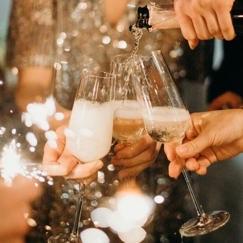 A person pours Champagne into flutes with a firework sparkler in the background.